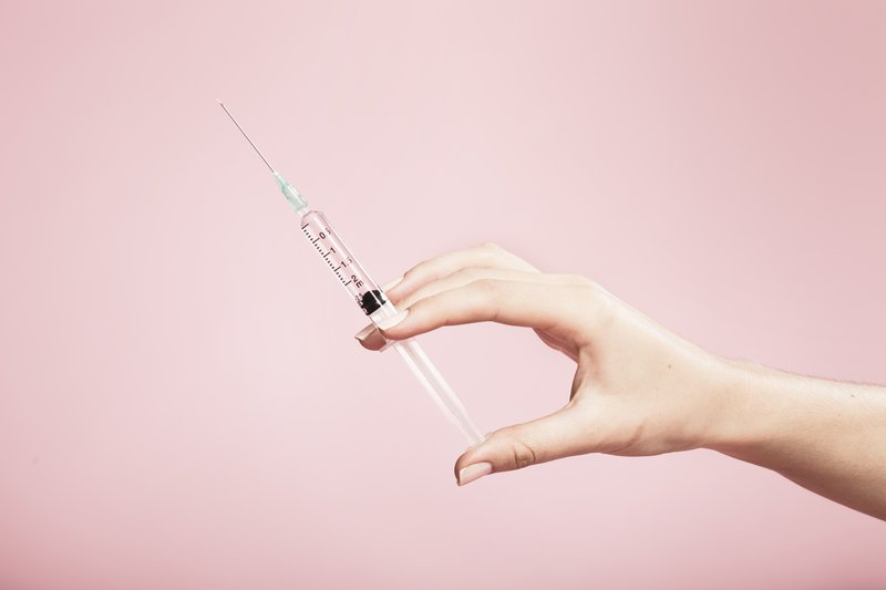 Hand holding syringe in plain pink background