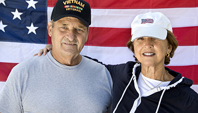 Vietnam Veteran and Wife looking at camera with American Flag in background