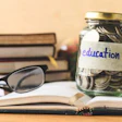 Coins in glass jar with education label, books,glasses and globe on wooden table. Financial concept.