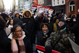 Large crowd of protesters marching in urban street with signs calling for political action during winter demonstration