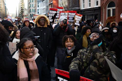 Large crowd of protesters marching in urban street with signs calling for political action during winter demonstration