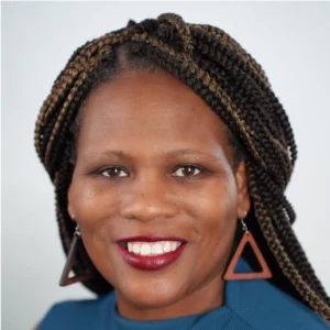 Professional headshot of a smiling woman with braided hair wearing a blue top and triangular earrings