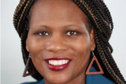 Professional headshot of a smiling woman with braided hair wearing a blue top and triangular earrings
