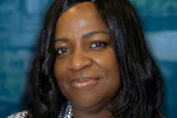 Professional headshot of a woman with long black hair smiling at the camera against a blurred blue background