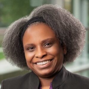 Professional headshot of a smiling woman with natural textured hair wearing a dark blazer