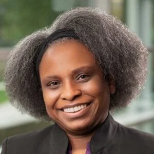 Professional headshot of a smiling woman with natural textured hair wearing a dark blazer