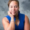 Professional headshot of woman in blue sleeveless top against gray background