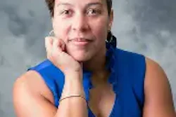 Professional headshot of woman in blue sleeveless top against gray background