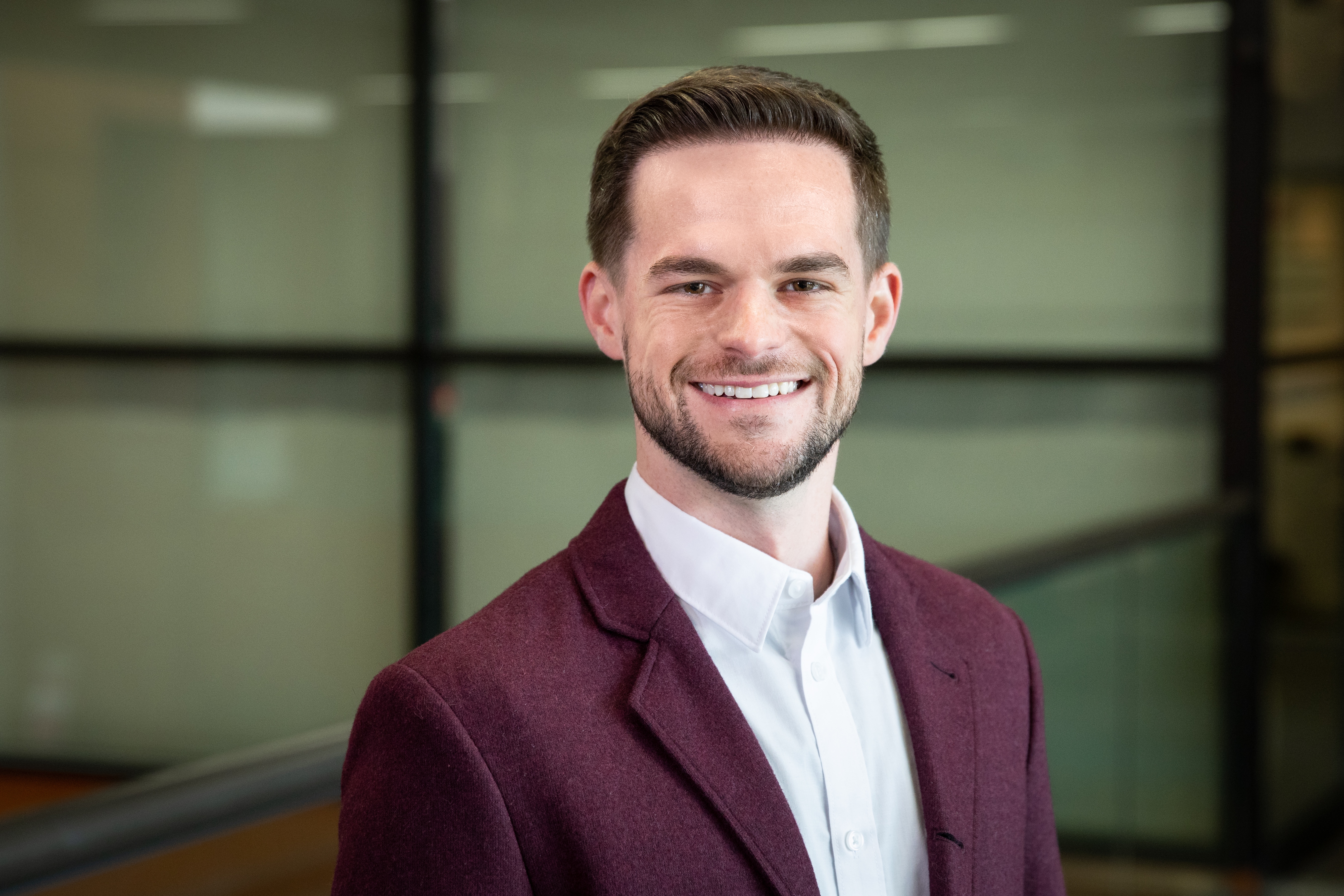 Professional man in maroon blazer and white shirt smiling in modern office setting