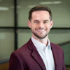 Professional man in maroon blazer and white shirt smiling in modern office setting