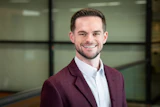 Professional man in maroon blazer and white shirt smiling in modern office setting