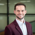 Professional man in maroon blazer and white shirt smiling in modern office setting