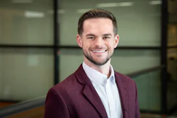 Professional man in maroon blazer and white shirt smiling in modern office setting
