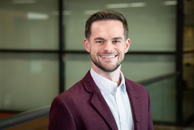 Professional man in maroon blazer and white shirt smiling in modern office setting
