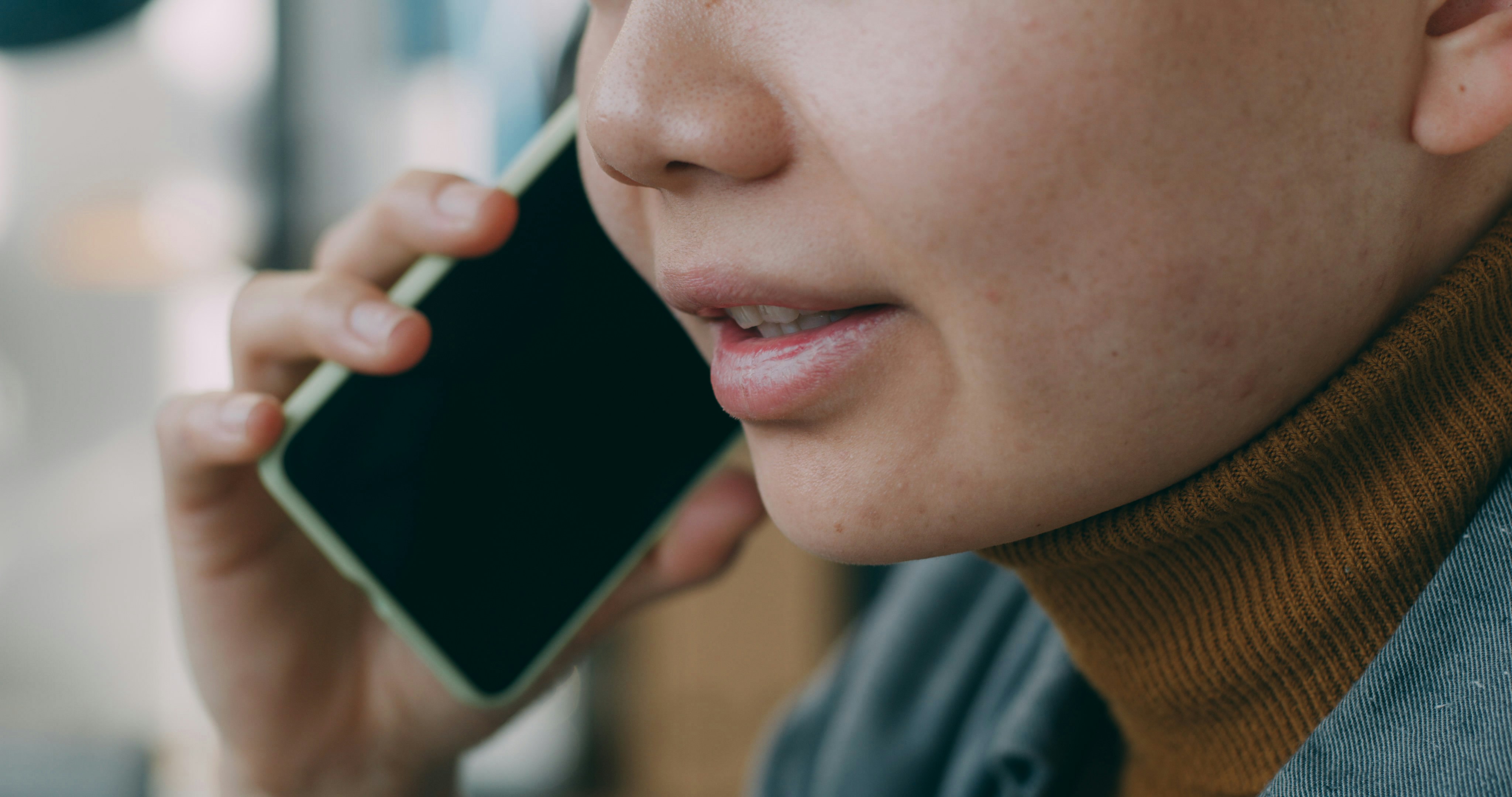 Person in brown turtleneck holding smartphone to ear during phone call