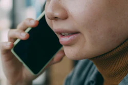 Person in brown turtleneck holding smartphone to ear during phone call