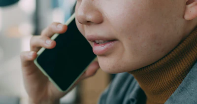 Person in brown turtleneck holding smartphone to ear during phone call