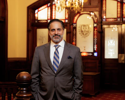 Professional man in gray suit and blue striped tie standing in elegant interior with wooden cabinetry