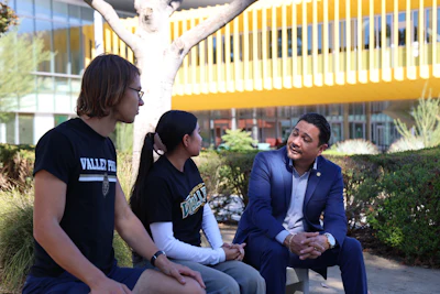 Three people conversing outdoors near a modern yellow building with landscaping