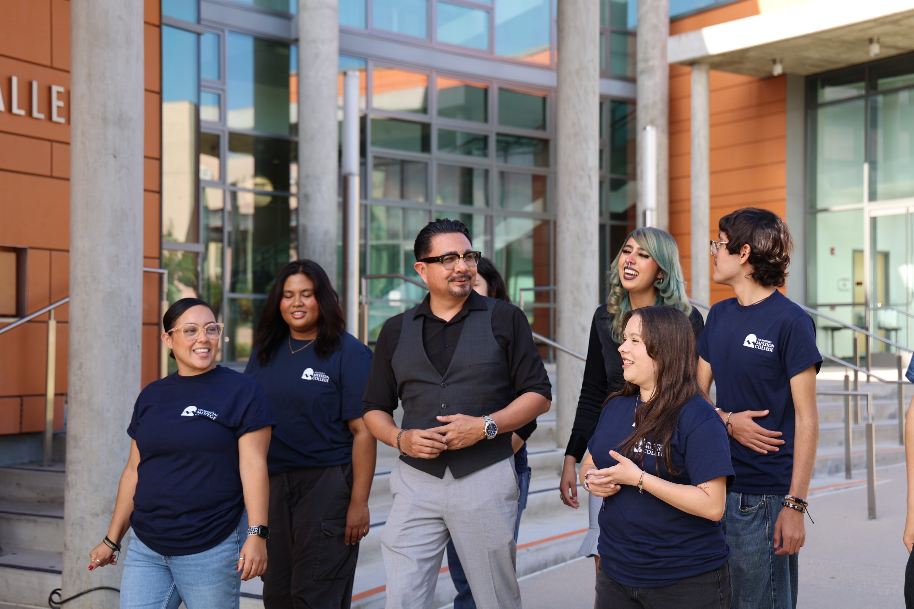 Group of six diverse professionals wearing matching navy branded t-shirts standing together outside a modern building with orange and concrete architecture