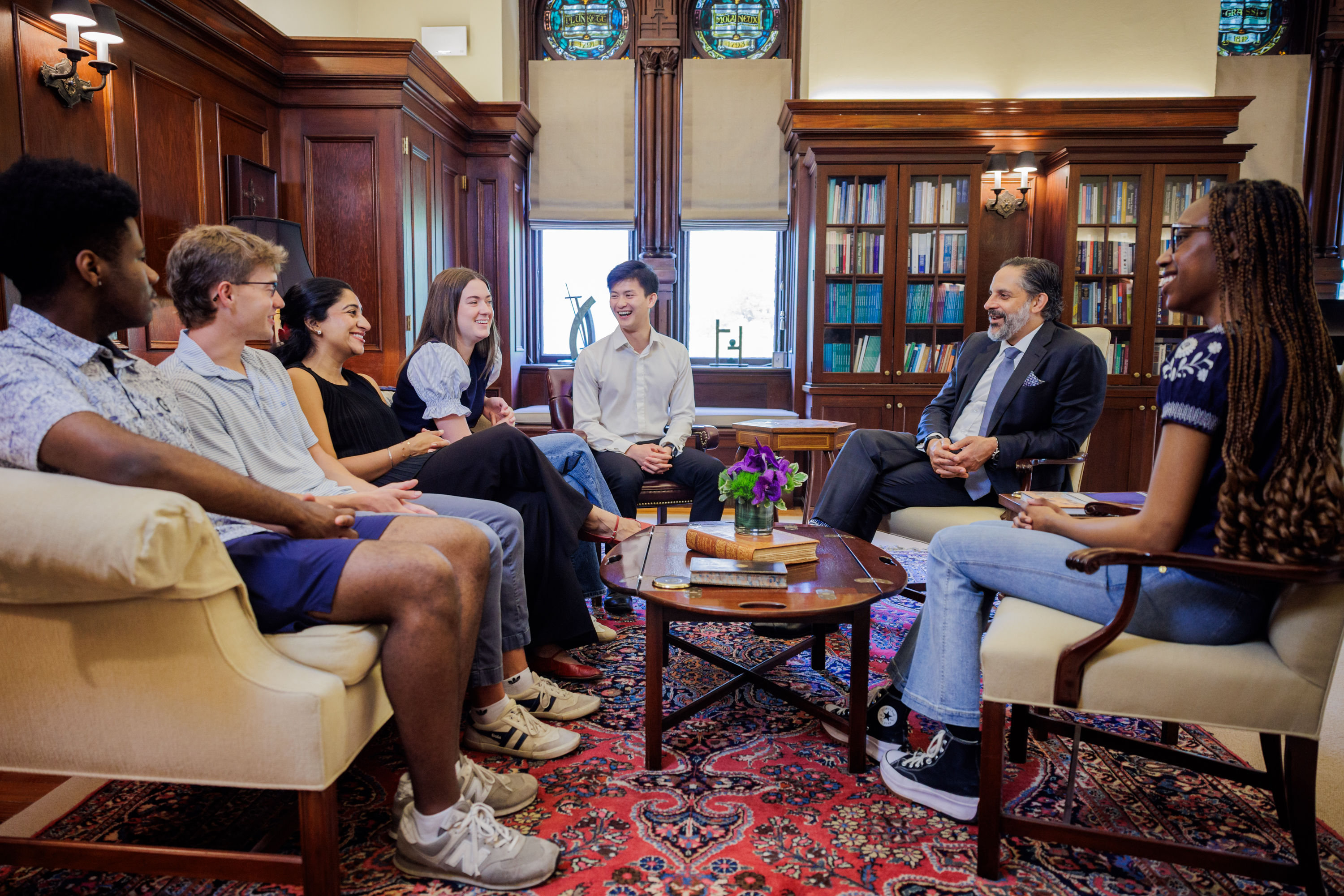 Group of diverse professionals engaged in discussion in an elegant wood-paneled library with bookshelves and ornate furnishings.