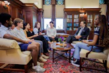 Group of diverse professionals engaged in discussion in an elegant wood-paneled library with bookshelves and ornate furnishings.