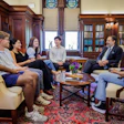 Group of diverse professionals engaged in discussion in an elegant wood-paneled library with bookshelves and ornate furnishings.