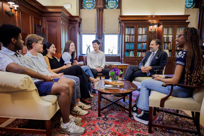 Group of diverse professionals engaged in discussion in an elegant wood-paneled library with bookshelves and ornate furnishings.