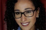 Smiling woman wearing glasses and striped sweater in warm indoor setting