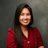 Professional headshot of smiling woman with long dark hair wearing red blazer against gray background