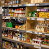 Food pantry shelves stocked with canned goods, pasta, potatoes, and packaged items organized by category