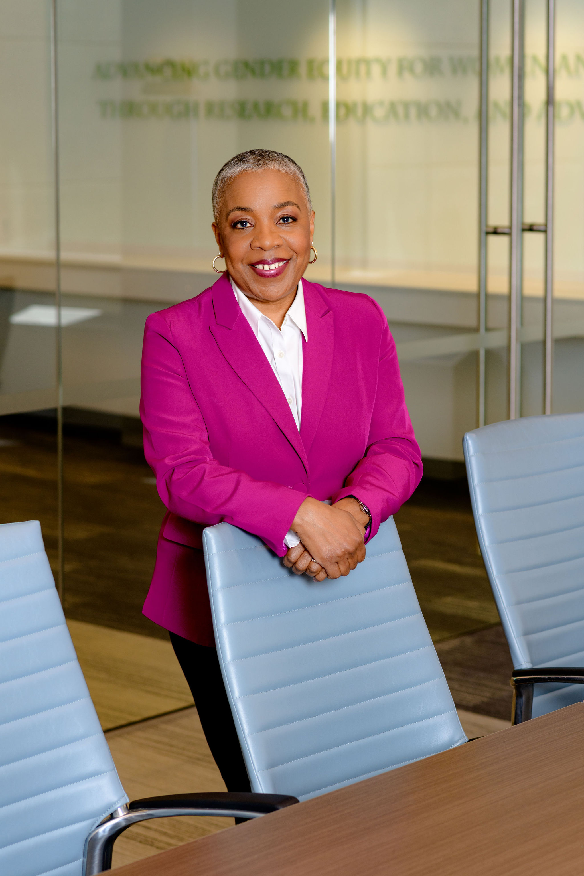 Professional woman in magenta blazer smiling at conference table in modern office