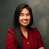 Professional headshot of a smiling woman with long dark hair wearing a burgundy blazer against a gray background