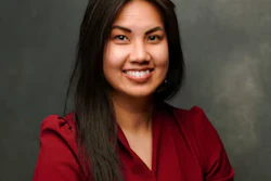 Professional headshot of a smiling woman with long dark hair wearing a burgundy blazer against a gray background