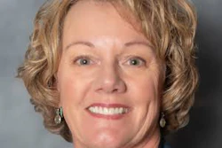 Professional headshot of a smiling woman with short blonde hair wearing a dark blue blazer and pearl earrings