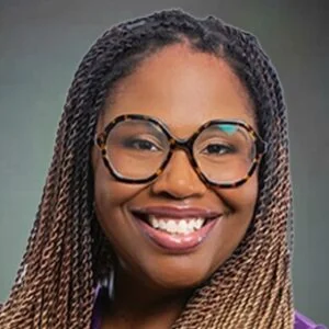 Professional headshot of a smiling woman wearing glasses and purple top