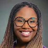 Professional headshot of a smiling woman wearing glasses and purple top
