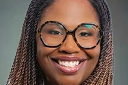 Professional headshot of a smiling woman wearing glasses and purple top