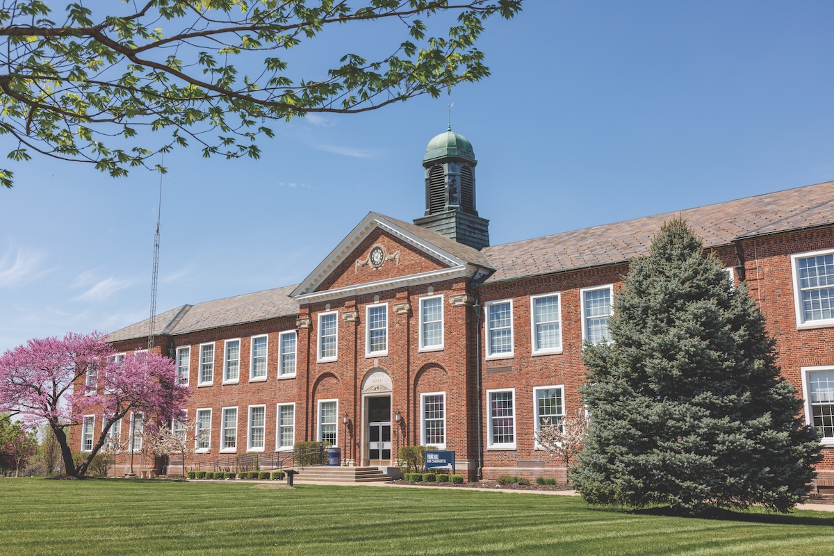 Historic red brick institutional building with green cupola and manicured lawn on clear spring day