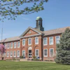 Historic red brick institutional building with green cupola and manicured lawn on clear spring day