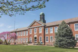 Historic red brick institutional building with green cupola and manicured lawn on clear spring day