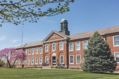 Historic red brick institutional building with green cupola and manicured lawn on clear spring day