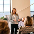 Professional woman presenting to colleagues in modern office with floor-to-ceiling windows and contemporary decor