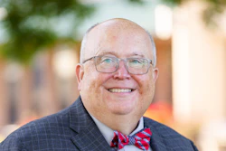 Professional headshot of a smiling man wearing glasses, navy plaid suit, light blue shirt, and red plaid bow tie