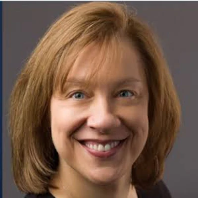 Professional headshot of a smiling woman with reddish-brown hair against a gray background