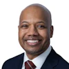 Professional headshot of a smiling man in business attire with dark suit and burgundy tie