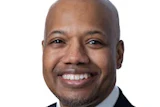Professional headshot of a smiling man in business attire with dark suit and burgundy tie