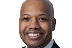 Professional headshot of a smiling man in business attire with dark suit and burgundy tie