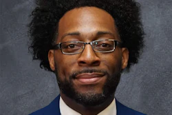 Professional headshot of a man wearing glasses, dark blue blazer, white shirt, and orange-blue striped tie against gray background