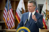California governor speaking at podium with state seal and American flag in background